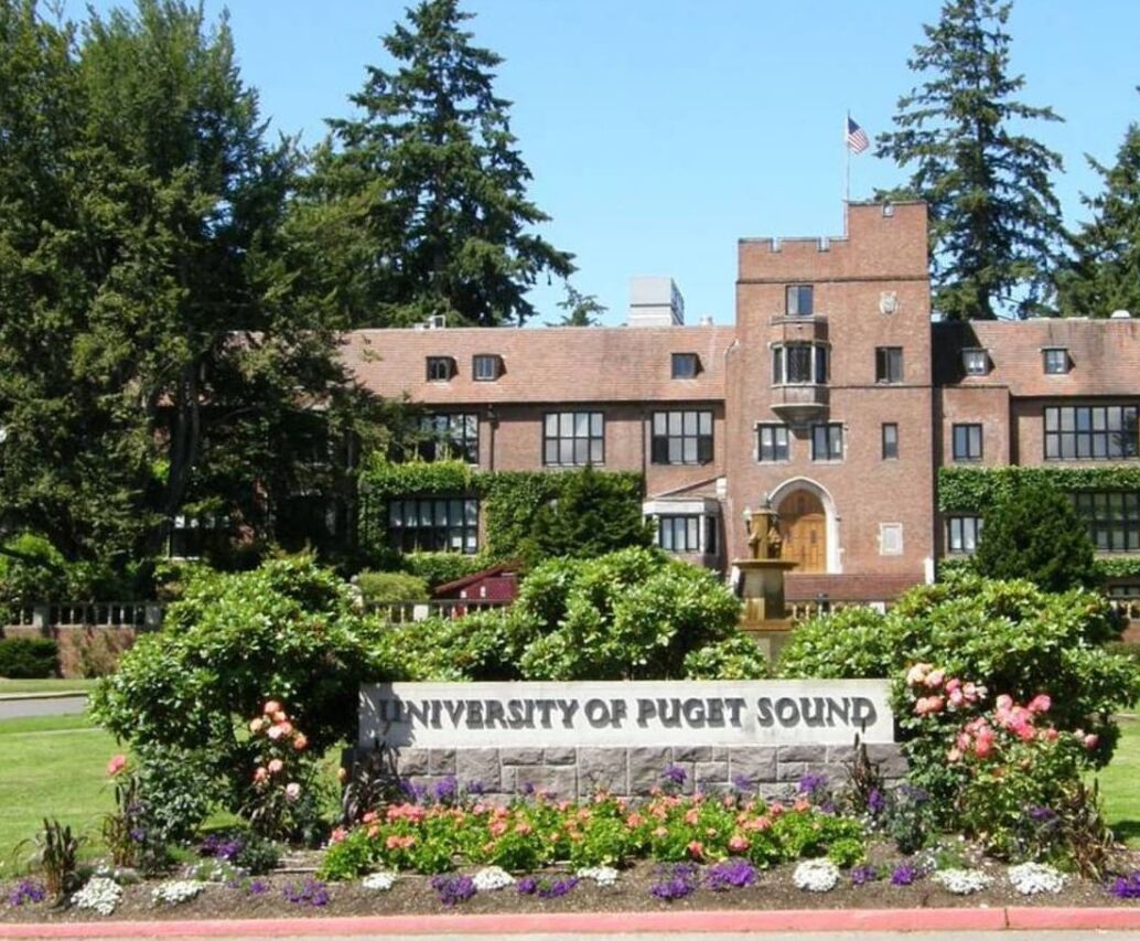 The University of Puget Sound's main building surrounded by lush greenery and a well-maintained garden.