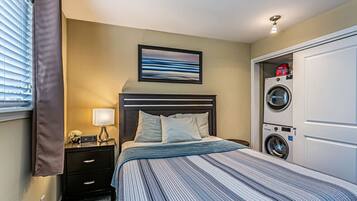 Habitación de hotel con cama, mesita de noche, lámpara, un cuadro enmarcado y lavadora secadora incorporada.