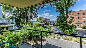 A balcony with a view of a parking lot, a brick building, and a tree.