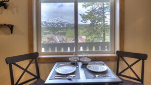 A dining table set with plates, cutlery, and glasses, positioned by a window with a view of a mountain and houses. - Beautifully Renovated Condo, Steps From Main St & Gondola; Very Clean (Breckenridge)