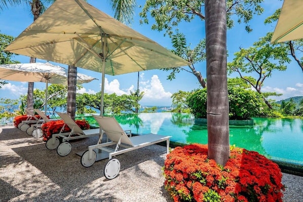 A poolside area with lounge chairs and umbrellas, surrounded by greenery and a clear view of the water.