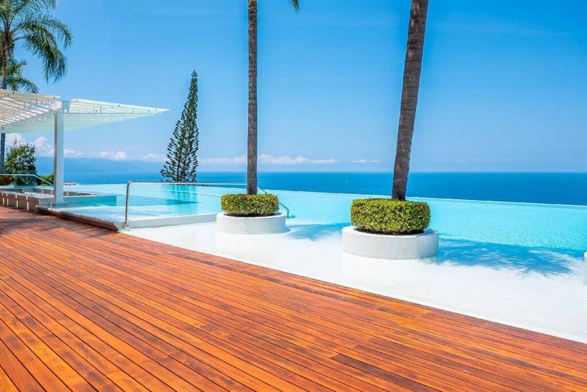 Eine Holzterrasse mit Pool und Palmen, mit Blick auf den klaren, blauen Ozean.