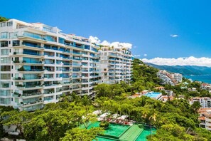 A multi-story hotel with balconies, a swimming pool, and lush greenery.