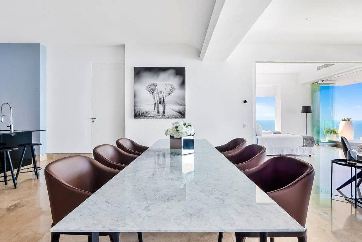 Ein moderner Essbereich mit einem Marmortisch, Ledersesseln und einem großen gerahmten Bild an der Wand.