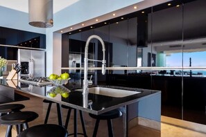A modern kitchen with a stainless steel sink, black bar stools, and a bowl of green apples.
