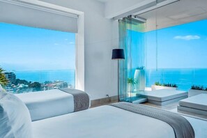 A modern hotel room with a large balcony, a glass partition, and a view of the sea.