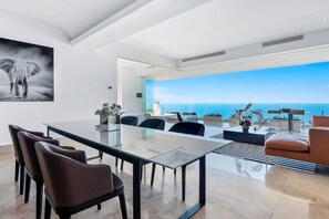 A modern interior with a dining area, a large window with a view of the ocean, and a painting of an elephant.