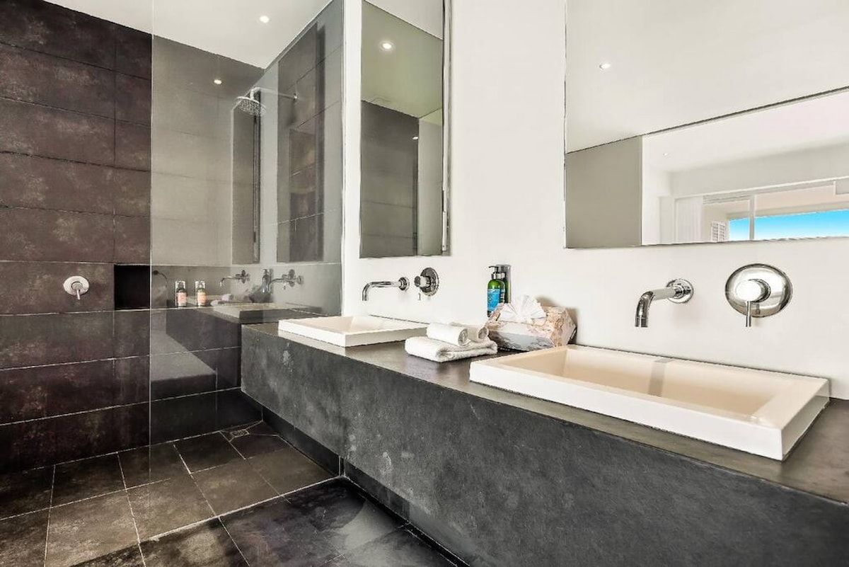 A modern bathroom with two sinks, a large mirror, and a shower.