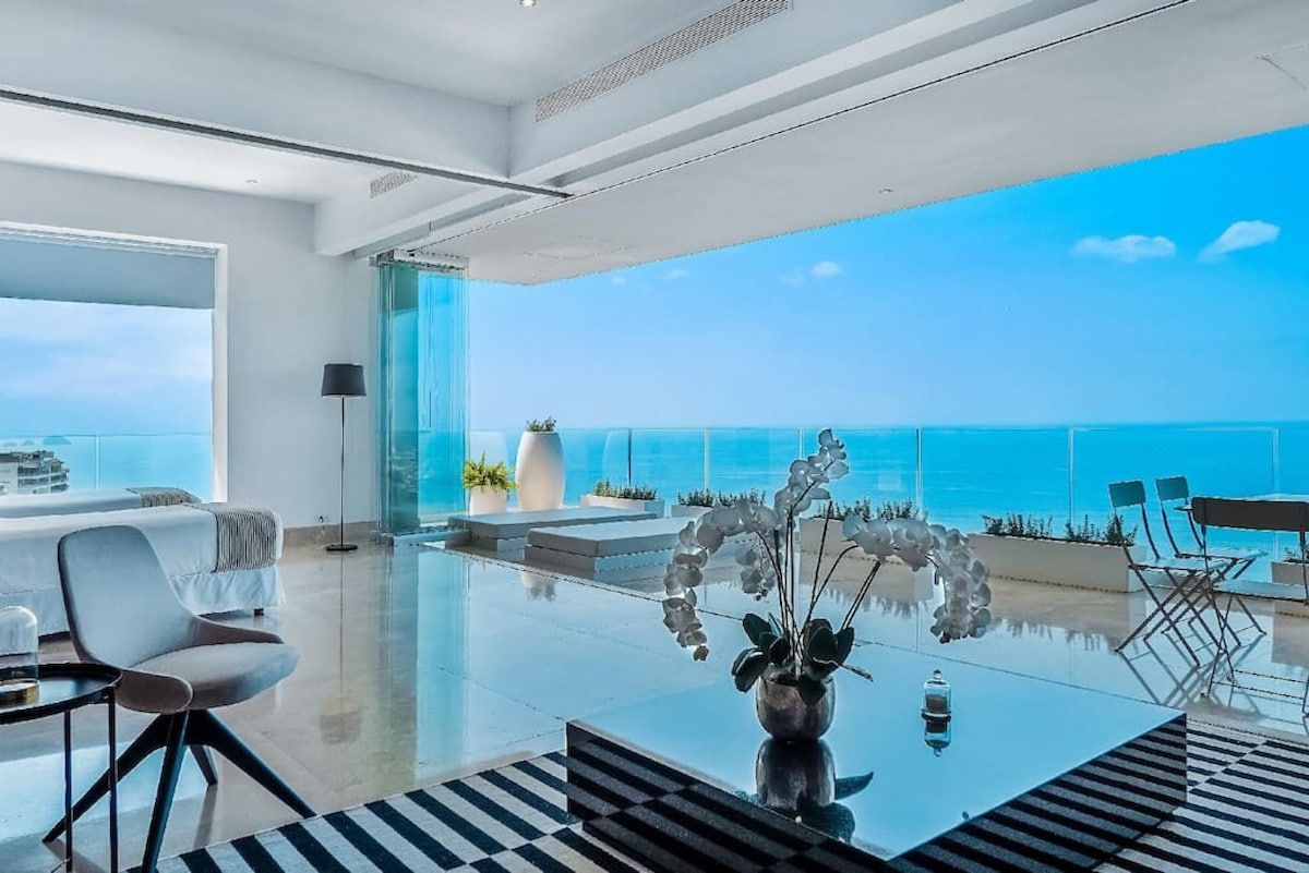 Un salon moderne doté d’un plancher en verre, d’un canapé, d’une table basse et offrant une vue sur l’océan.