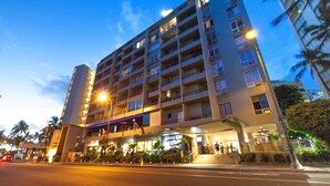 Un hotel de varios pisos con entrada central, balcones y fachada bien iluminada.