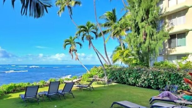 A hotel with a view of the ocean, palm trees, and outdoor seating areas.