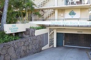 The exterior of the Diamond Head Beach Hotel & Resort, featuring a stone wall, a sign with the address, and a closed garage door.
