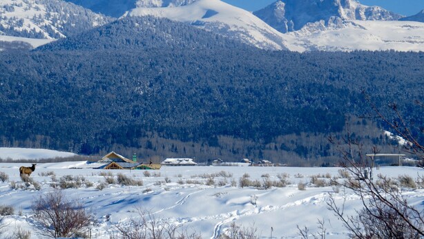 Paisagem coberta de neve, com montanhas ao fundo e uma pequena cabana em primeiro plano.
