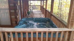 Een hottub in een houten terras met uitzicht op bomen.