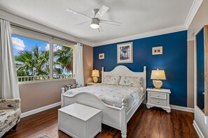 A bedroom with a bed, bedside tables, a chair, a ceiling fan, and a view of palm trees through the window. - 4th Flr 1 Bdrm+Bunks/2Bath. Upgraded! Sleeps 6 (Panama City Beach)