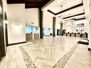 A spacious lobby with a herringbone patterned floor, large pillars, and a reception desk.