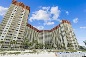 A high-rise hotel with multiple balconies, a beach view, and palm trees.
