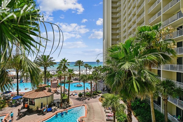 A hotel with a pool area, palm trees, and a view of the beach.