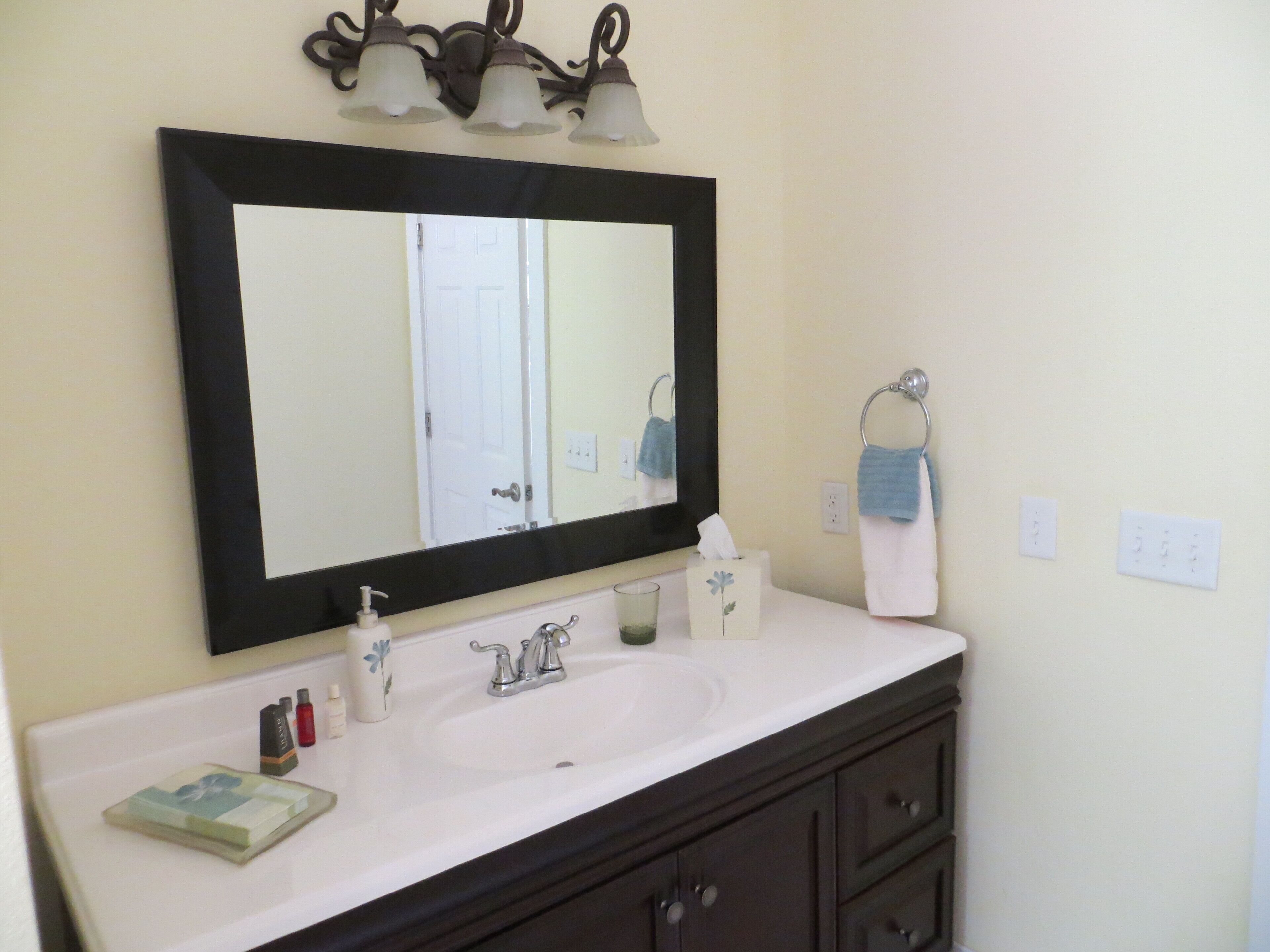 A bathroom with a white sink, dark wooden vanity, a large mirror, and a towel rack.