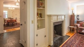 Una habitación con chimenea, una estantería, un comedor con mesa y sillas, y una alfombra estampada.