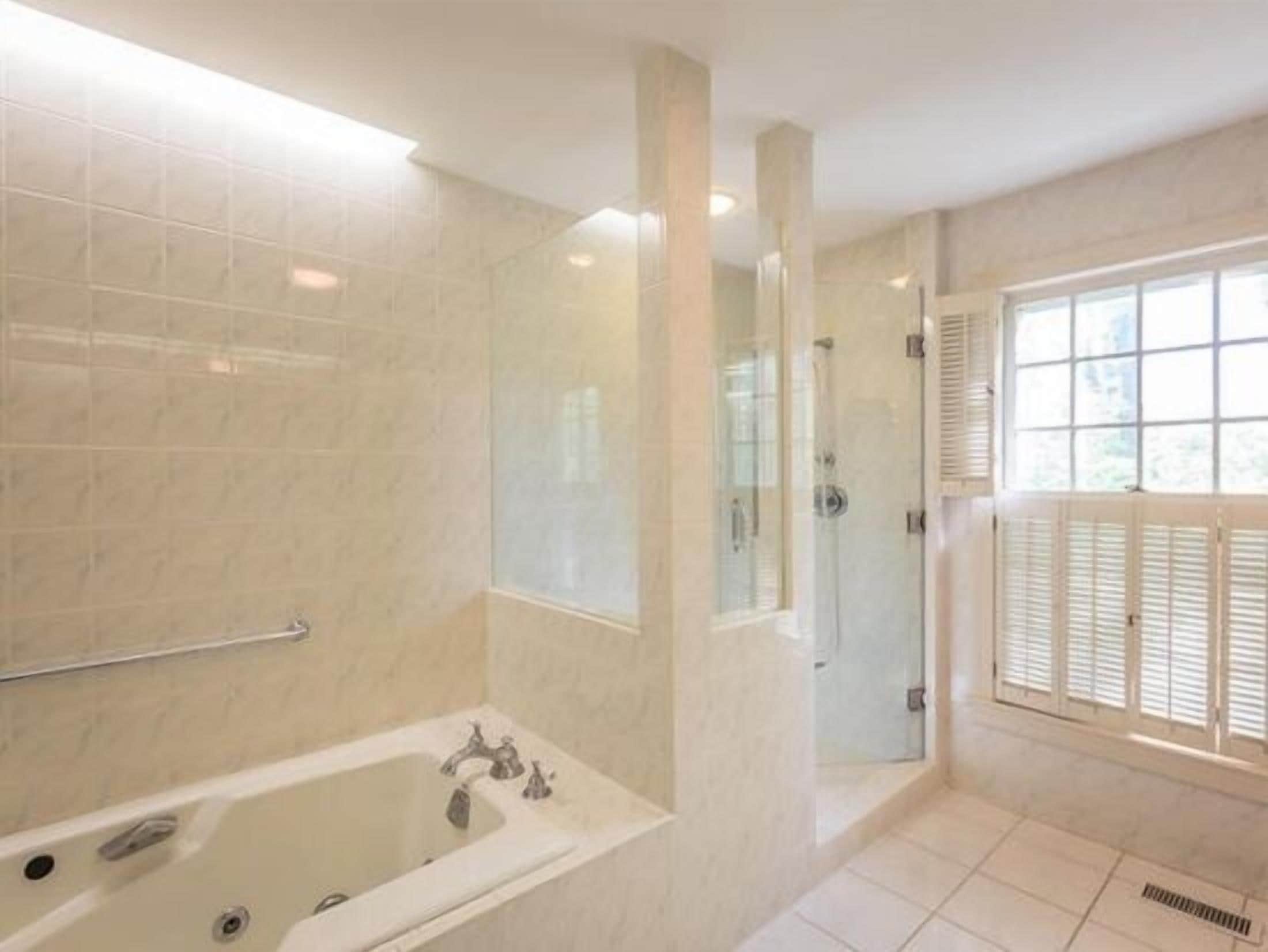 Un baño con bañera, cabina de ducha de vidrio y ventana con contraventanas.