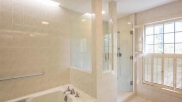 Un baño con bañera, cabina de ducha de vidrio y ventana con contraventanas.