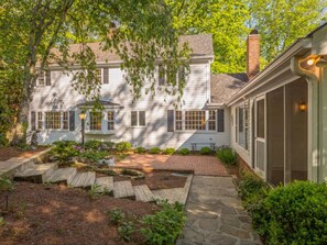 A two-story house with a front porch, stone pathway, and a garden with various plants.