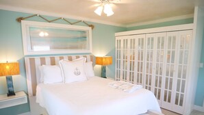 A neatly arranged bedroom with a bed, bedside lamps, a framed artwork, and a wardrobe. - Sailor's Rest, a Romantic and Luxurious Sanctuary  (Christiansted)