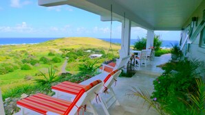 A covered outdoor seating area with white chairs and red cushions, overlooking a lush landscape and the ocean. - Sailor's Rest, a Romantic and Luxurious Sanctuary  (Christiansted)