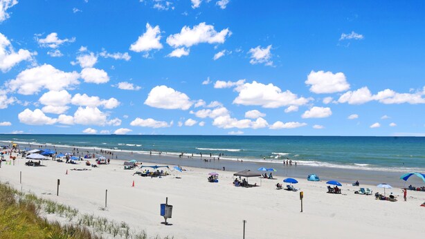 Ein Strand mit Sonnenschirmen, Menschen und blauem Himmel.