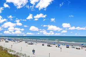 A beach with umbrellas, people, and a clear sky.