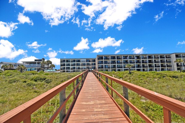 A wooden boardwalk leading to a modern building with multiple balconies.
