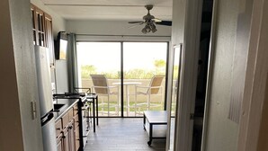 Ein schmaler Flur führt zu einem Balkon mit Deckenventilator, einem kleinen Tisch mit Stühlen und Blick ins Freie.