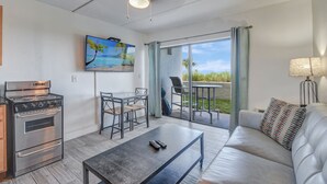 Eine moderne Küche mit integriertem Backofen und Herd, ein Essbereich mit Tisch und Stühlen, eine Couch mit einem gemusterten Kissen und ein großes Fenster mit Blick ins Freie.