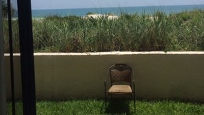 Ein Balkon mit Stuhl und Tisch, der Blick auf einen Strand mit Gras und einem klaren Himmel bietet.