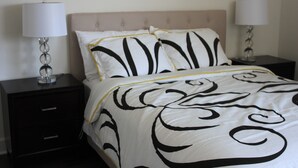 Un letto rifatto con cura, con copriletto bianco e nero, due comodini con lampade e un comodino scuro con cassetti.