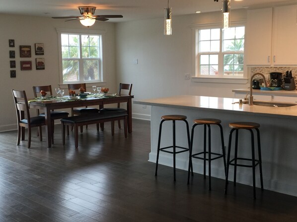 A modern kitchen with a dining area, wooden flooring, and a ceiling fan.
