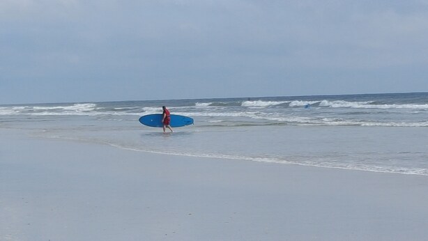 Ein Strand mit einer Person, die einen blauen Surfbrett trägt.