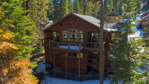 Una cabaña de madera de varios pisos con un balcón, rodeada de árboles y nieve.