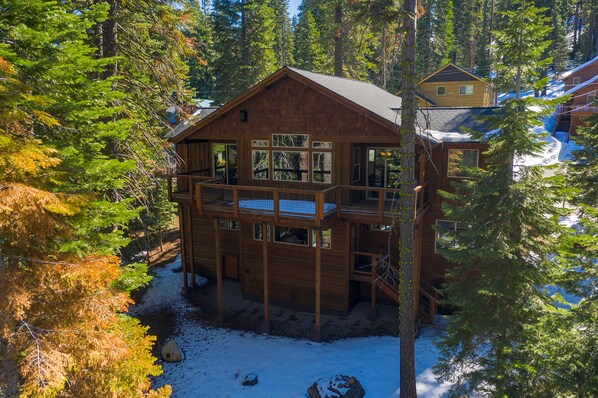 A multi-story wooden cabin with a balcony, surrounded by trees and snow.