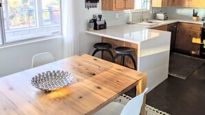 A modern kitchen with wooden cabinets, a white countertop, and a bar stool. - Stunning Views: Rockwood Hill House (Joshua Tree)