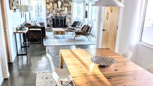 A modern living room with a stone fireplace, a dining area with a wooden table and chairs, and a cozy seating area with a sofa and armchairs. - Stunning Views: Rockwood Hill House (Joshua Tree)