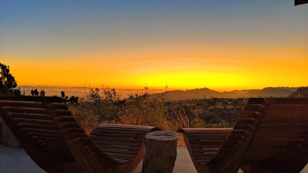 A sunset view from a terrace with wooden benches and a central stone table. - Stunning Views: Rockwood Hill House (Joshua Tree)