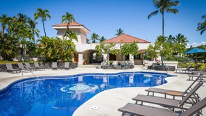 A resort pool area with lounge chairs, palm trees, and a building with a red-tiled roof. -  SPECTACULAR !!  Ground Floor Condo Sleeps 5  Golf ,Tennis ,.Gym Pool, Jacuzzi (waikoloa village)