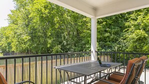 Une terrasse couverte avec une table et des chaises, une clôture en bois et une végétation luxuriante en arrière-plan.