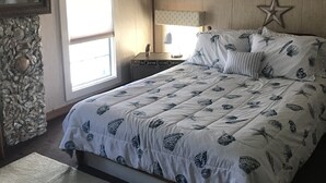 A bedroom with a sloped ceiling, a bed with a nautical-themed duvet, a star decoration on the wall, and a stone accent wall.