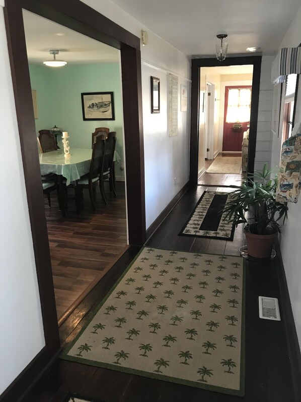 Un pasillo con suelo de madera, un comedor con mesa y sillas, y una planta en maceta.