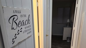Um corredor com piso de madeira, uma porta branca e uma placa com a inscrição 'A caminhada na praia vale mais que mil palavras'.