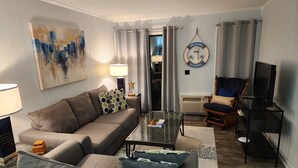 Uma sala de estar com sofá, poltrona, mesa de centro, televisão e obras de arte.