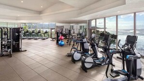 Un gimnasio espacioso con máquinas de cardio, equipo de levantamiento de pesas y vistas panorámicas al océano.